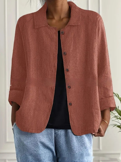 Person wearing a brown jacket over a black top and blue jeans indoors.