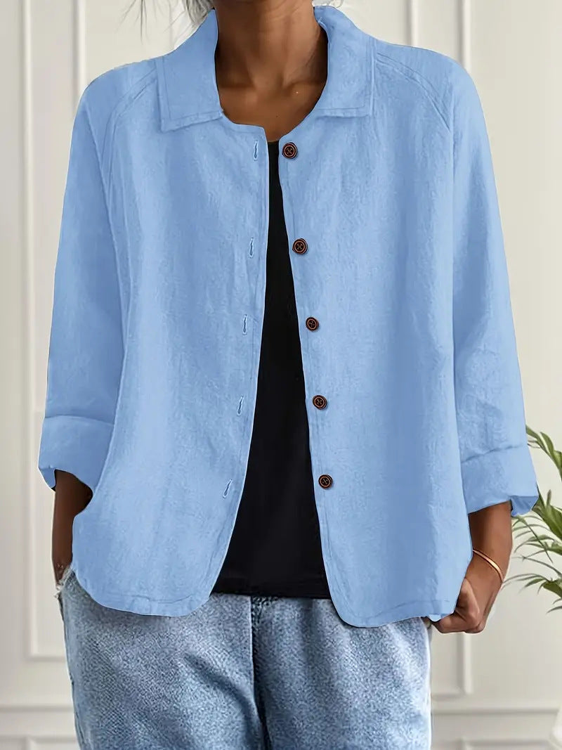 Person wearing a light blue jacket with brown buttons against a white wall.