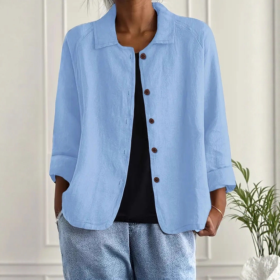 Person wearing a light blue jacket with brown buttons against a white wall.