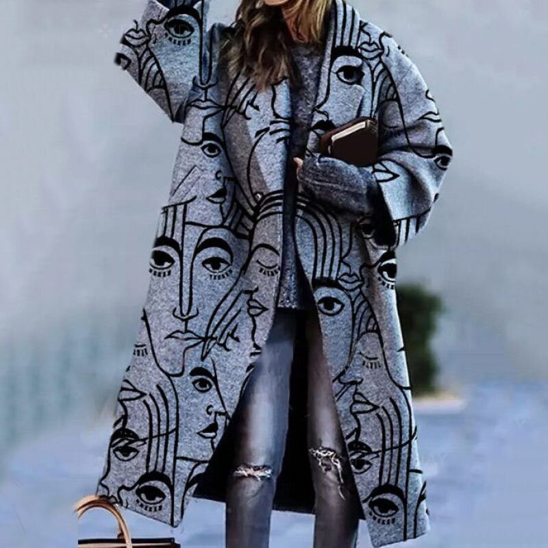 Grijze lange jas met abstract gezichtenprint, gedragen door vrouw buiten | Boutique Moda