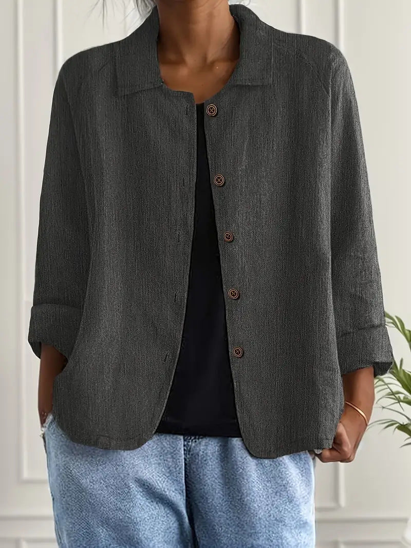 Person wearing a gray blazer over a black top and blue jeans indoors.