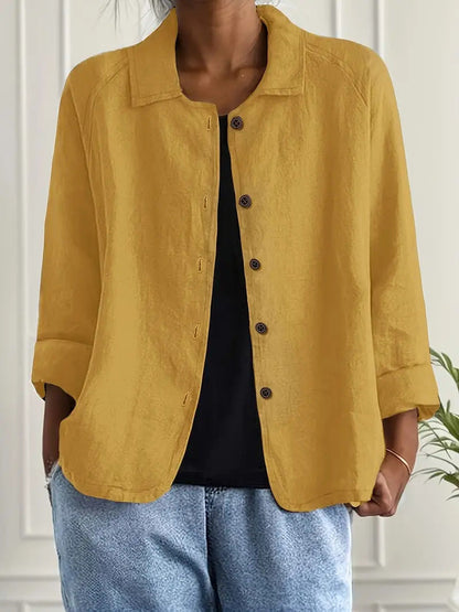Person wearing a mustard yellow jacket over a black top and blue jeans indoors.